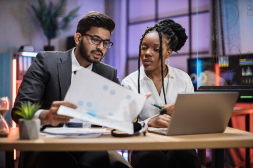 Two professionals sit at a desk and discuss plans for a CMMC assessment
