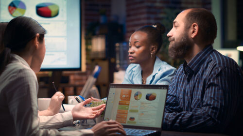 Coworkers sit with a laptop and discuss revenue figures